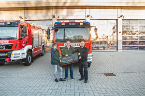 Zu sehen sind links die Leiterin des Sachgebiets Infrastruktur und mittig der Brandschutzbeauftragte des Kreises Schleswig-Flensburg, Gunnar Brast, wie sie die Löschdecke am Standort Friedrichsberg der Schleswiger Feuerwehr an den Wehrführer Sönke Schloßmacher, rechts im Bild, übergeben.