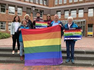 Sieben Personen hinter einer Regenbogenflagge