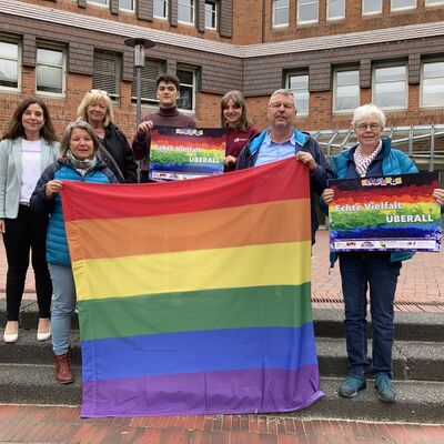 Sieben Personen hinter einer Regenbogenflagge