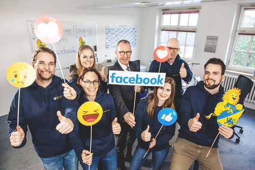 Das Social Media Team des Kreises und Landrat Doktor Buschmann halten das Facebook-Logo und typische Reaktionszeichen von Facebook hoch