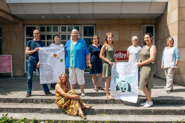 Die Kursleitung Gerald Nack und Wiebke Schneider, Anja Heldt, Brigitte Halfen, Fachdienstleiterin Carmen Marxen, Stefanie Monsee, Vorsitzende des Jugendhilfeausschusses des Kreises Karin Carstensen und Projektbeauftragte des Kreises für das Bundesprogramm ProKindertagespflege Jasmin Empen und Claudia Kilian stehen auf einem Treppenabsatz und halten Plakate in der Hand.
