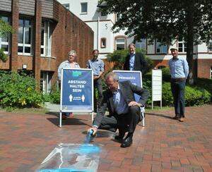 Landrat Dr. Buschmann sprayt eine Bodenschablone.
