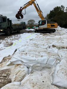 Bagger hebt ein sogenanntes Bigpack von einem Transporter, um das Loch im Deich zu stopfen.