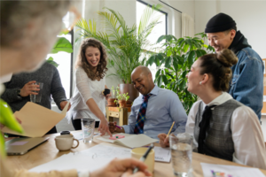 Verschiedene Personen sitzen oder stehen gemeinsam an einem Tisch und tauschen sich aus