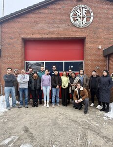 16 M&auml;nner und Frauen stehen vor dem Feuerwehrhaus und l&auml;cheln