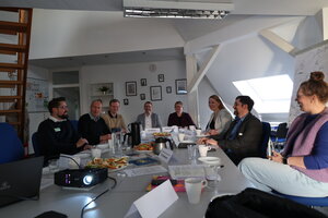 8 M&auml;nner und Frauen sitzen gemeinsam zum Gespr&auml;ch an einem Tisch