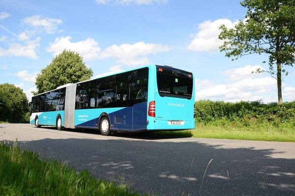 Ein t&uuml;rkis-blau-beklebter Bus steht auf einer Stra&szlig;e vor einem Feld