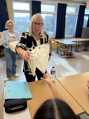 Eine blonde Frau &uuml;berreicht eine Schult&uuml;te.
